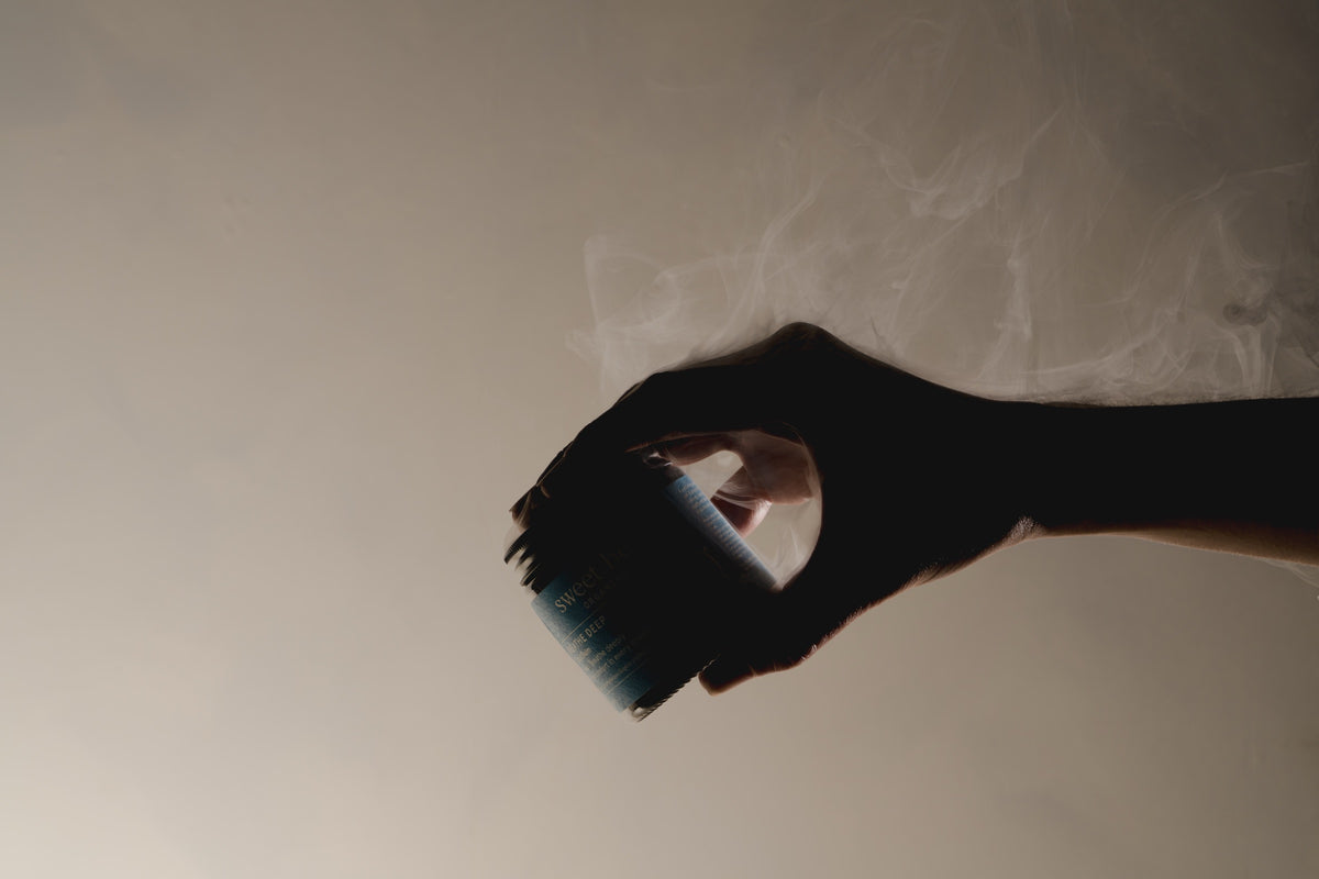 A hand holding the Breathe Deep Cloud Balm jar in soft vapour