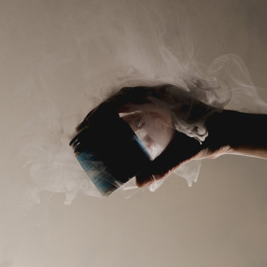 A hand holding the open Breathe Deep Cloud Balm jar with vapor rising