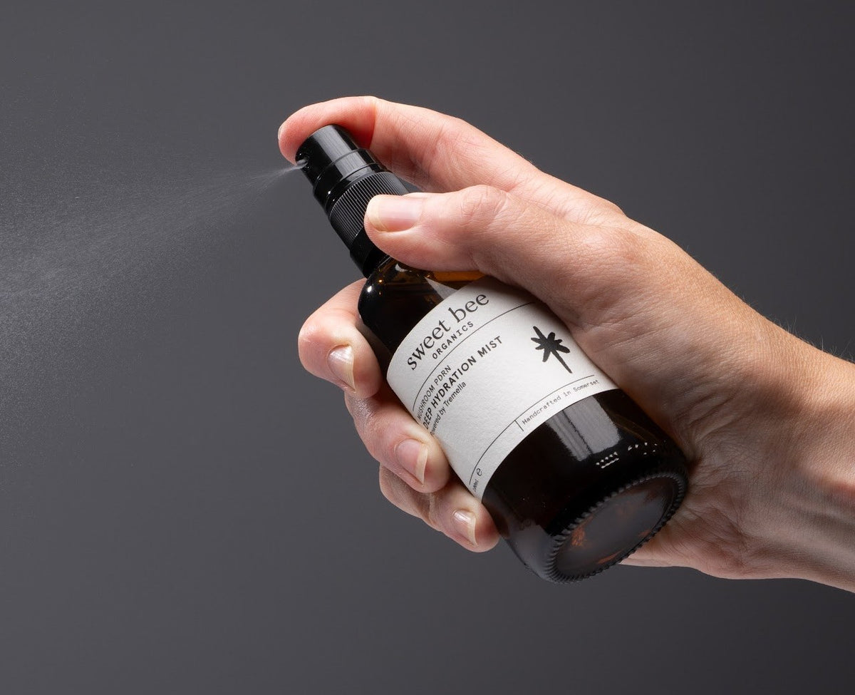 A hand misting Deep Hydration Mist, the spray lit against a dark background